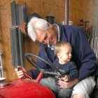 Un agricultor veterano muestra a su nieto los mandos de un viejo tractor en una explotación agraria