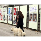 Una mujer pasea tranquilamente con su perro ante los carteles electorales, en Bilbao.-LUIS TEJIDO / EFE