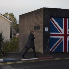 Una mujer pasa junto a un muro que luce la bandera de la Union Jack, en el barrio de Fountain West, en la localidad norirlandesa de Derry.-ALBERT BERTRAN