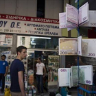 Ciudadanos griegos pasean ante carteras con el diseño del euro en un quiosco del centro de Atenas, este martes.-