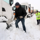 Un camionero retenido en el polígono de Aguilar de Campoó (Palencia), retira nieve de su camión para poder reanudar la marcha-Ical