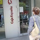 Una clienta se topa con la oficina de Caja España cerrada y lee el cartel que informa de ello en la puerta.-J.M. Lostau