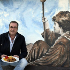 César Acero, con un plato del menú, junto al mural de temática jacobea de su complejo hostelero-ARGICOMUNICACIÓN