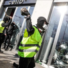 Un chaleco amarillo rompe el cristal de una tienda en los Campos Elíseos de París.-GEOFFROY VAN DER HASSELT (AFP)