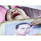 Una mujer llora a las puertas del hospital con la la foto del rey Bhumibol.-EFE / DIEGO AZUBEL