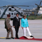 Renzi, Merkel y un oficial tratan de ajustar la alfombra roja en el aeropuerto de Nápoles, antes de desplazarse a Ventotene.-AFP / MARIO LAPORTA