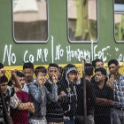 Grupos de refugiados piden continuar su viaje, junto a una valla frente al tren detenido, este viernes en Bcske.-EFE / BALAZS MOHAI