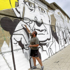 Un artista pinta la cara de Miguel Delibes en el mural de la Avenida Salamanca, en dirección al Puente de la Hispanidad-J. M. Lostau