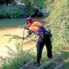 Un voluntario en la búsqueda en el río y el cartel de desaparición.-E. M.