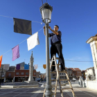 El párroco de Villalón, Francisco Casas, coloca los banderines en la plaza junto a El Rollo, tras haber instalado un gran cartel de ‘Holywins’.-J. M. LOSTAU