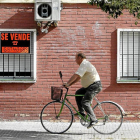 Un hombre en bicicleta pasa por delante de un cartel de 'Se vende' en una vivienda.-Carlos Márquez