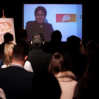 El expresidente de la Generalitat, Carles Puigdemont, conversa por videoconferencia con candidatos y simpatizantes durante la inauguración de la sede de campaña de Junts per Catalunya.-EFE