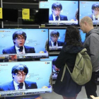Una pareja sigue la rueda de prensa de Puigdemont en una tienda del Poblenou.-/ FERRAN NADEU