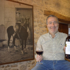 Ricardo Rodilla enseña una botella en el interior de la bodega tradicional ante la mirada de una foto de su madre, Társila a caballo.-ARGICOMUNICACIÓN