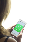 Una chica mira la pantalla de su teléfono móvil, con el logo de Whatsapp.-EL PERIÓDICO