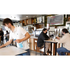 Un camarero desinfecta la mesa en el Café Villa de Prado el día antes del cierre del interior de la hostelería mientras unos clientes disfrutan de su consumición. / J.M. LOSTAU