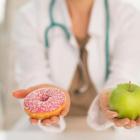Una doctora dando a elegir entre un donut o una manzana.-123RF