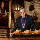 Alberto Cándido López, hijo del mesonero Cándido, con los cochinillos asados que han dado la vuelta al mundo, sobre las andas, y un retrato de su padre detrás, en el Mesón de Cándido de Segovia.-ARGICOMUNICACIÓN