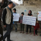 Niños sirios sostienen pancartas reivindicativas frente a miembros de un convoy de ayuda humanitaria durante una entrega de material en Al-Nashabia, en la región de Guta Oriental, al este de Damasco, el 28 de noviembre.-AFP / AMER ALMOHIBANY