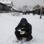 Un refugiado come en medio de la nieve en Belgrado.-REUTERS / MARKO DJURICA