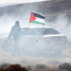 Un hombre ondea la bandera palestina entre gas lacrimógeno, este domingo durante una protesta en el pueblo cisjordano de Shiyoukh, cercano a Hebrón.-ABED AL HASHLAMOUN (EFE)