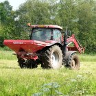 Un agricultor trabaja en un cultivo a bordo de un tractor con esparcidor de fertilizante