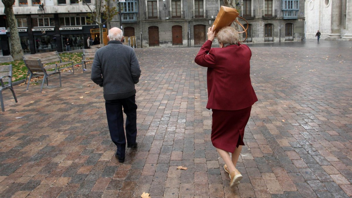 Una señora se protege de la lluvia con su bolso en la plaza de la Universidad