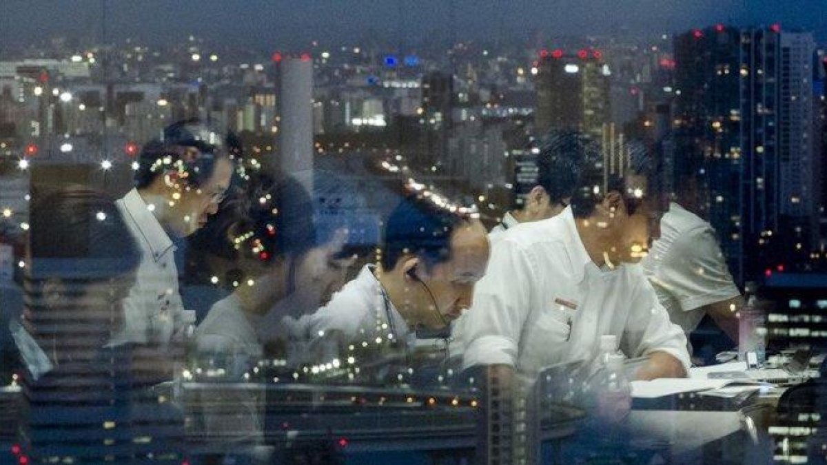 Empleados japoneses trabajando a altas horas de la noche en una empresa tecnológica con sede en Tokio.-THOMAS PETER (REUTERS)