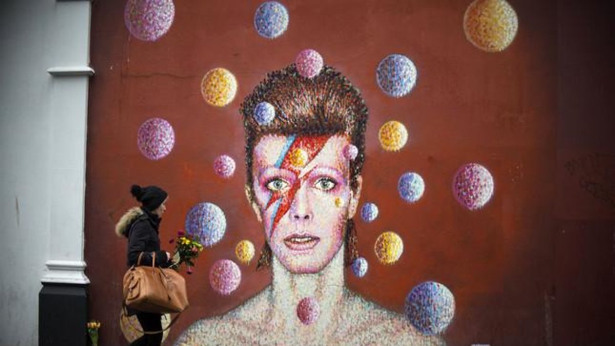 Flores ante un mural de David Bowie en la pared del comercio Morley, en Brixton (Londres), lugar de nacimiento del cantante.-