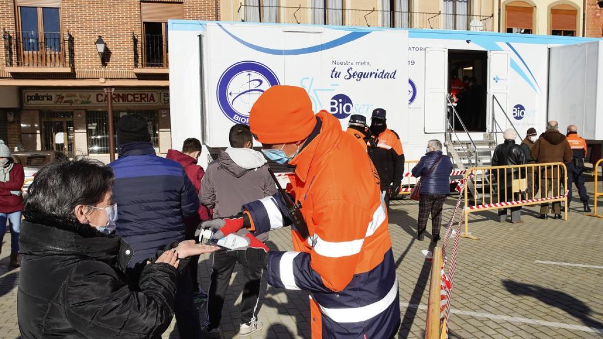 Un trabajador de Protección Civil echa gel hidroalcohólico a una mujer mientras espera en la cola para hacerse el test de antígenos. J.M. LOSTAU