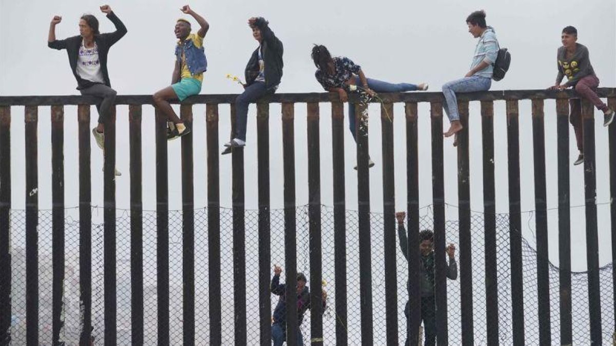 Miembros de la caravana de migrantes que cruzó México a pie hasta la frontera con Estados Unidos trepan el muro fronterizo que separa ambos países el pasado 29 de abril del 2018.-SANDY HUFFAKER (AFP)
