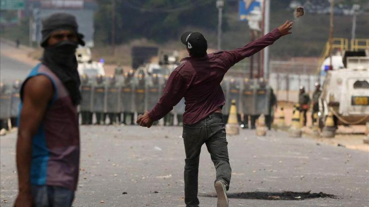 Un manifestante lanza una piedra contra policías venezolanos en la frontera con Brasil, este domingo. Un manifestante lanza una piedra contra policías venezolanos en la frontera con Brasil, este domingo.-REUTERS / BRUNO KELLY