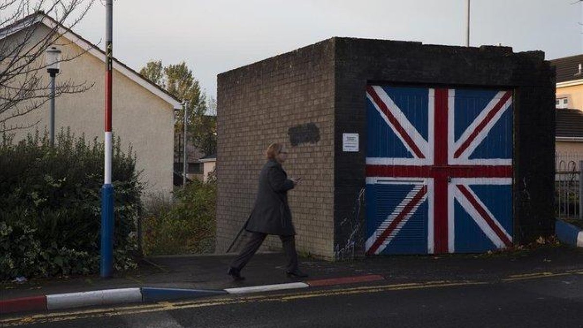 Una mujer pasa junto a un muro que luce la bandera de la Union Jack, en el barrio de Fountain West, en la localidad norirlandesa de Derry.-ALBERT BERTRAN