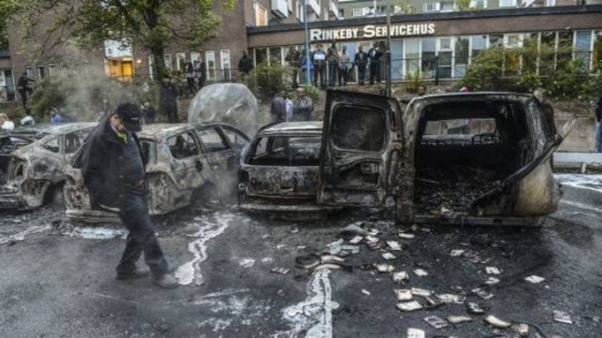Un hombre camina junto a una hilera de coches carbonizados tras unos disturbios en mayo del 2013, en un suburbio de Estocolmo.-Foto: EFE / FREDRIK SANDBERG