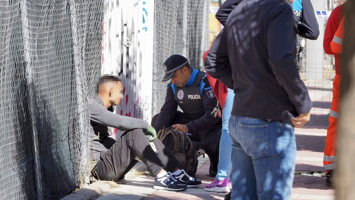 El joven que se encaramó a la grúa, sentado en la acera tras bajar, mientras un policía inspecciona la mochila. PHOTOGENIC
