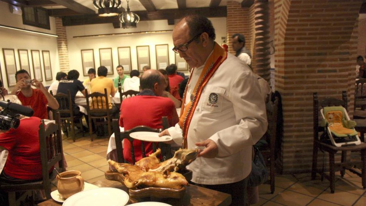 José María Ruiz trincha un cochinillo con un plato en una de las salas de su restaurante segoviano.-L.P.