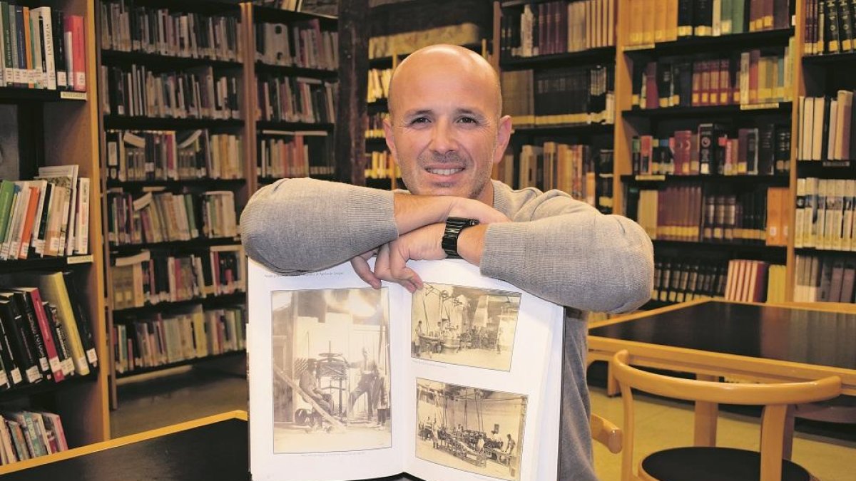 Enrique Bravo con un libro de fotografías antiguas que muestran el interior del obrador de Fontaneda en una de las salas de la biblioteca de Aguilar de Campoo.-E.M.