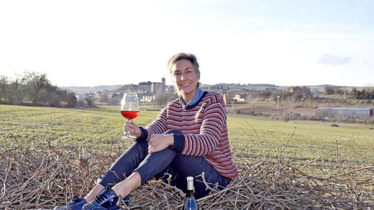 La enóloga María Pinacho se sienta sobre sarmientos mientras sujeta una copa de su vino en el paraje de los mimbreros, con el municipio de Mucientes al fondo.-ARGICOMUNICACIÓN