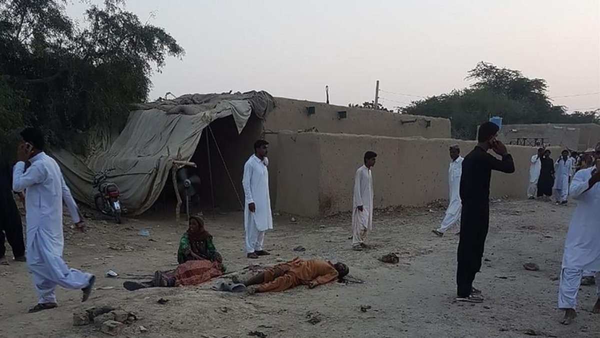 Algunos fieles deambulan junto a los cuerpos de las víctimas del atentado en Pakistán, este jueves-AFP