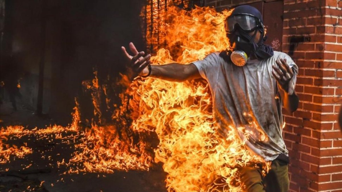 Un manifestante entre llamas después de estallar el depósito de la moto de un policía durante una protesta contra el presidente Maduro en Caracas.-JUAN BARRETO
