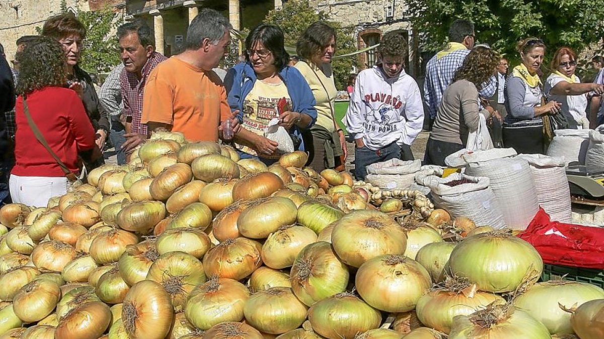 A la izquierda, compradores y curiosos conversan ante un expositor de cebollas en Palenzuela (Palencia). Arriba, cebollas asadas preparadas para una degustación.-BRÁGIMO