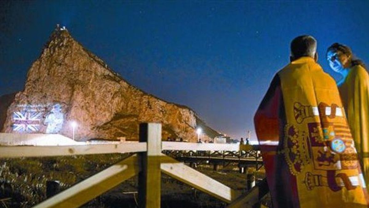 Una pareja mira desde la Línea de la Concepción la proyección de la imagen de Isabel II en el Peñón, en junio del 2012, cuando las autoridades de Gibraltar celebraron el 60º aniversario del ascenso al trono de la reina.-AFP / MARCOS MORENO