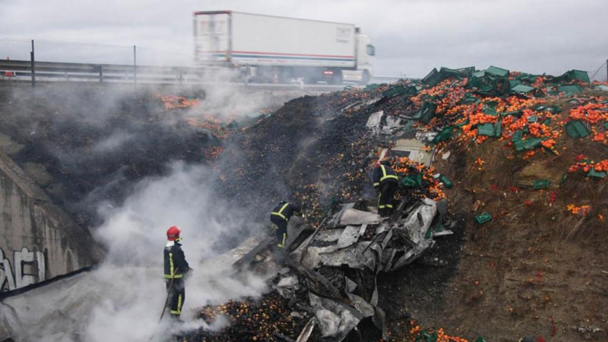 Los Bomberos apagan el fue del camión que quedó destrozado por el fuego y el impacto.-B. González