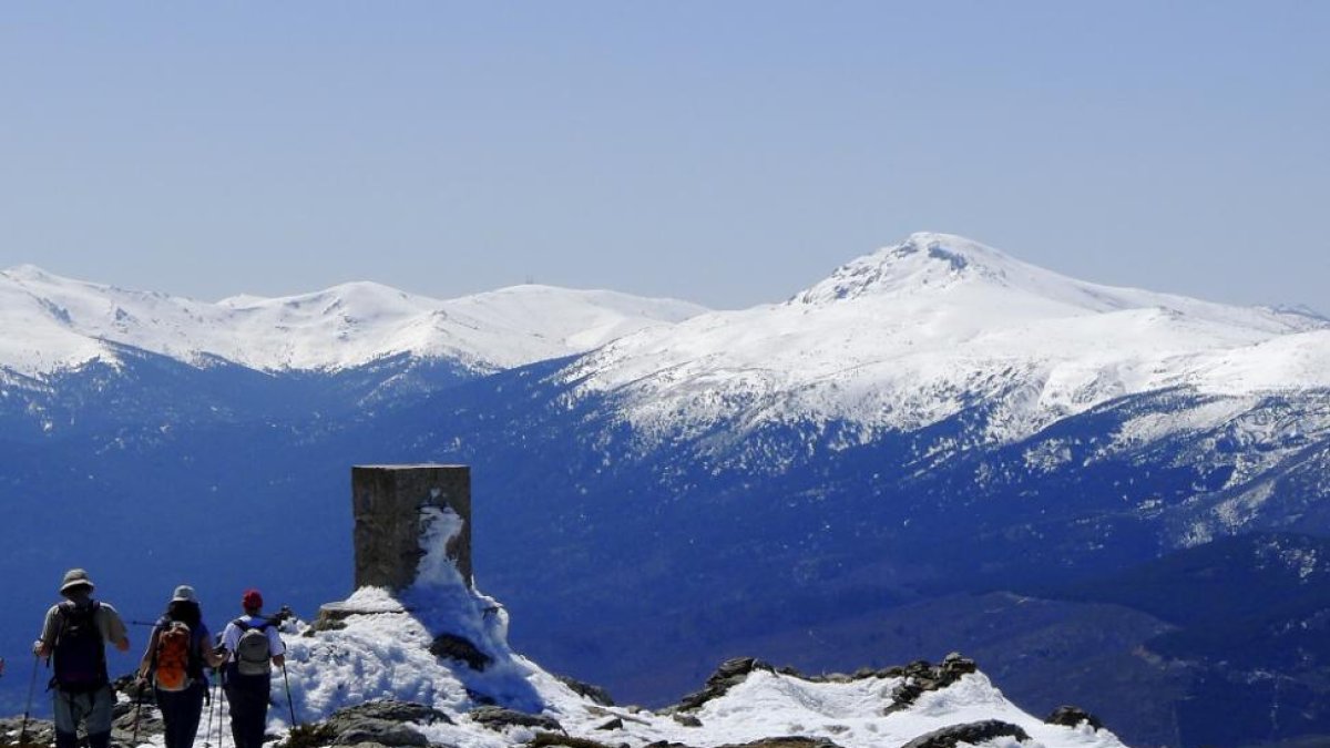 Un grupo de montañeros alcanza la cumbre del pico nevero, con el pico Peñalara al fondo.-N.S.