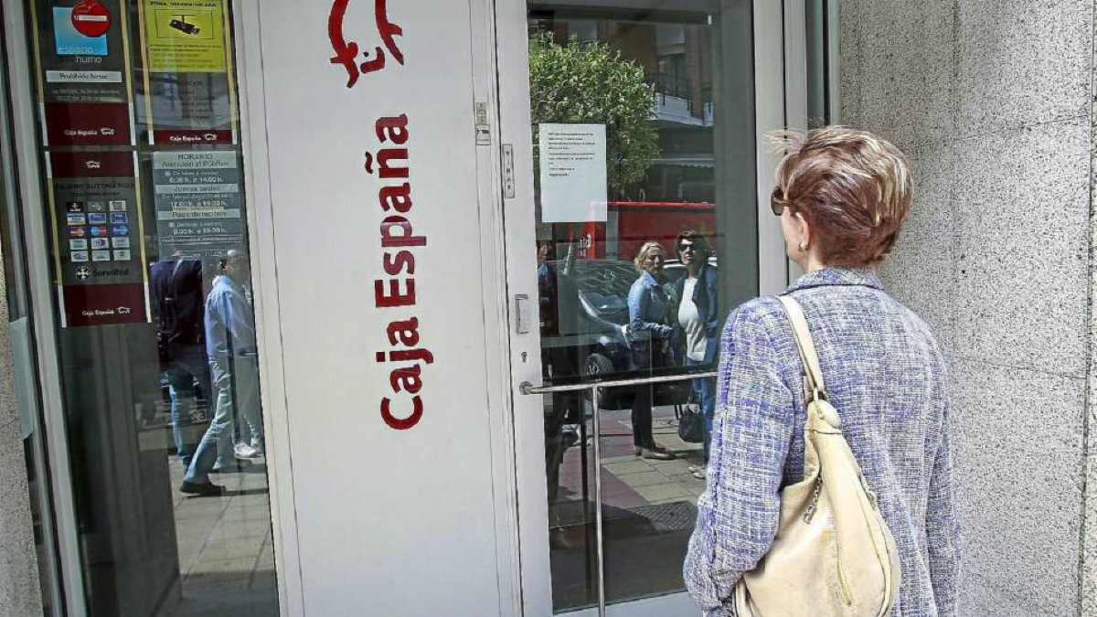 Una clienta se topa con la oficina de Caja España cerrada y lee el cartel que informa de ello en la puerta.-J.M. Lostau