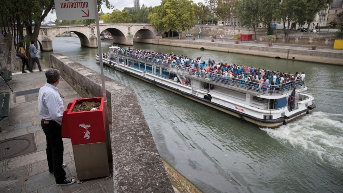 Un hombre utiliza un uritrottoir ante el paso de un bateau mouche en el Sena.-EL PERIÓDICO