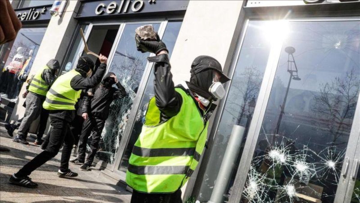 Un chaleco amarillo rompe el cristal de una tienda en los Campos Elíseos de París.-GEOFFROY VAN DER HASSELT (AFP)
