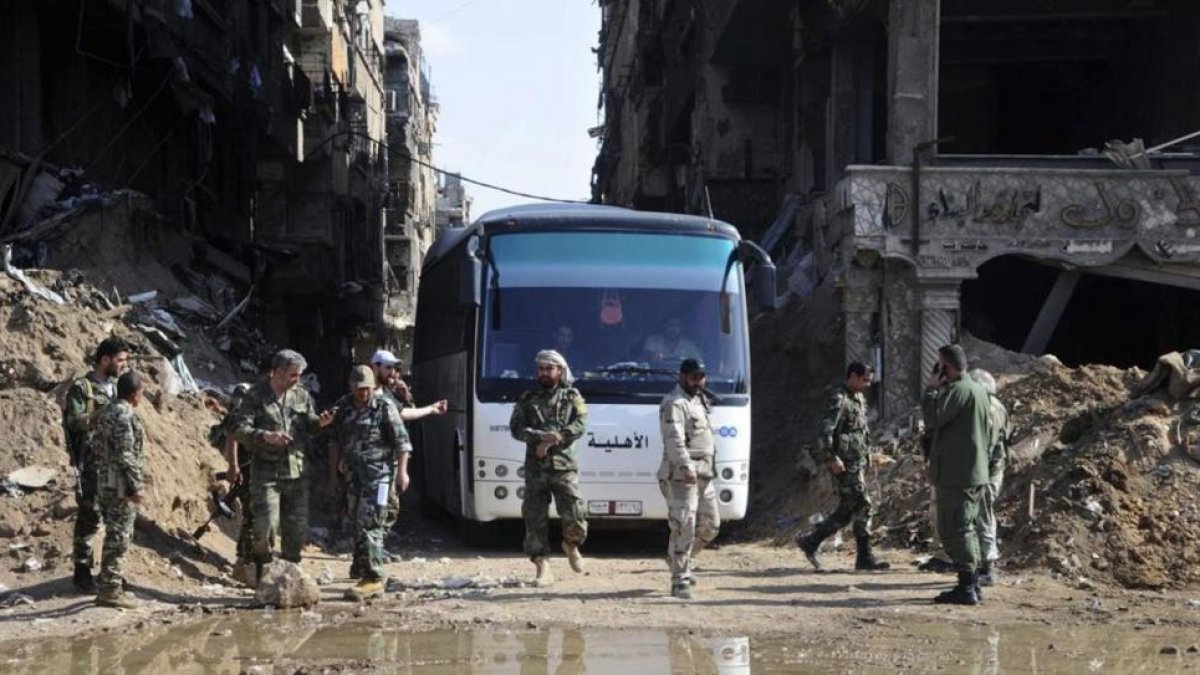 Militares del Ejército sirio supervisan un autobús que transporta combatientes vinculados a Al Qaeda durante una evacuación desde el campo de refugiados palestinos de Yarmuk, cerca de Damasc-SANA / AP