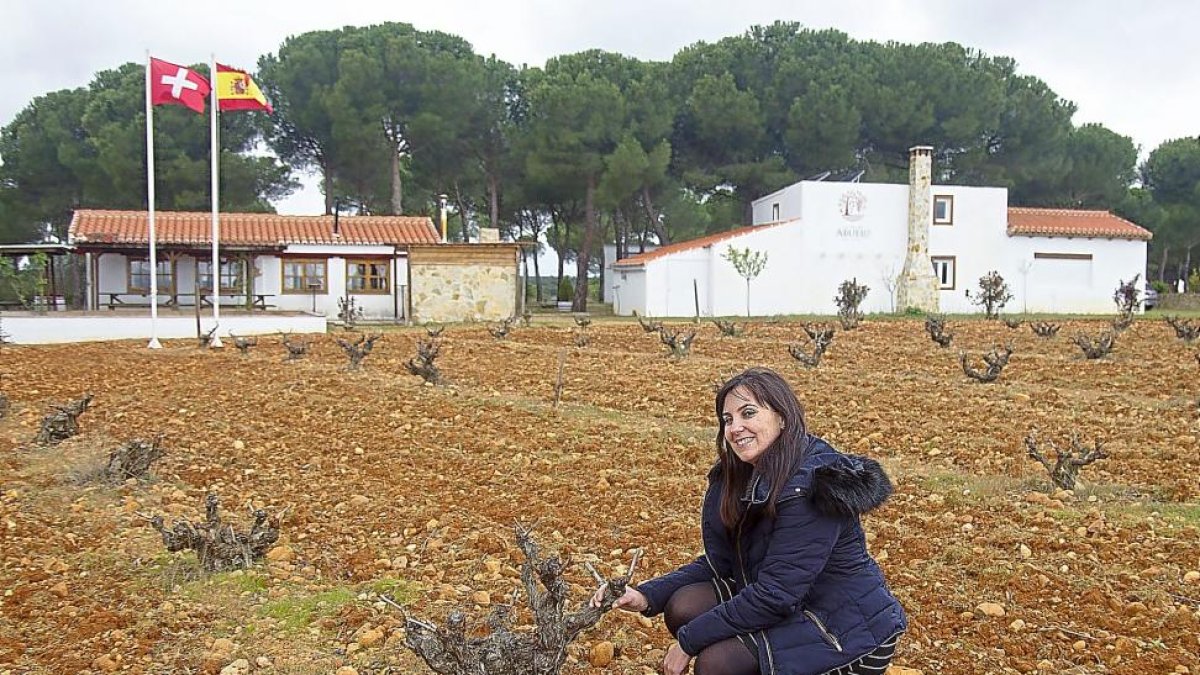 Ana Silvo posa sonriente con una cepa. Al fondo, la bodega y a la derecha lo vinos que comercializan.-M.D.