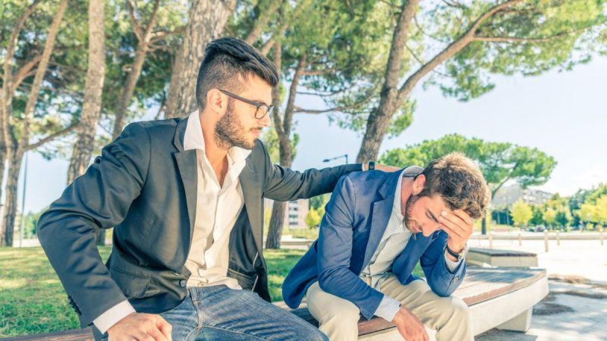 Un hombre consuela a otro en el banco de un parque.-123RF